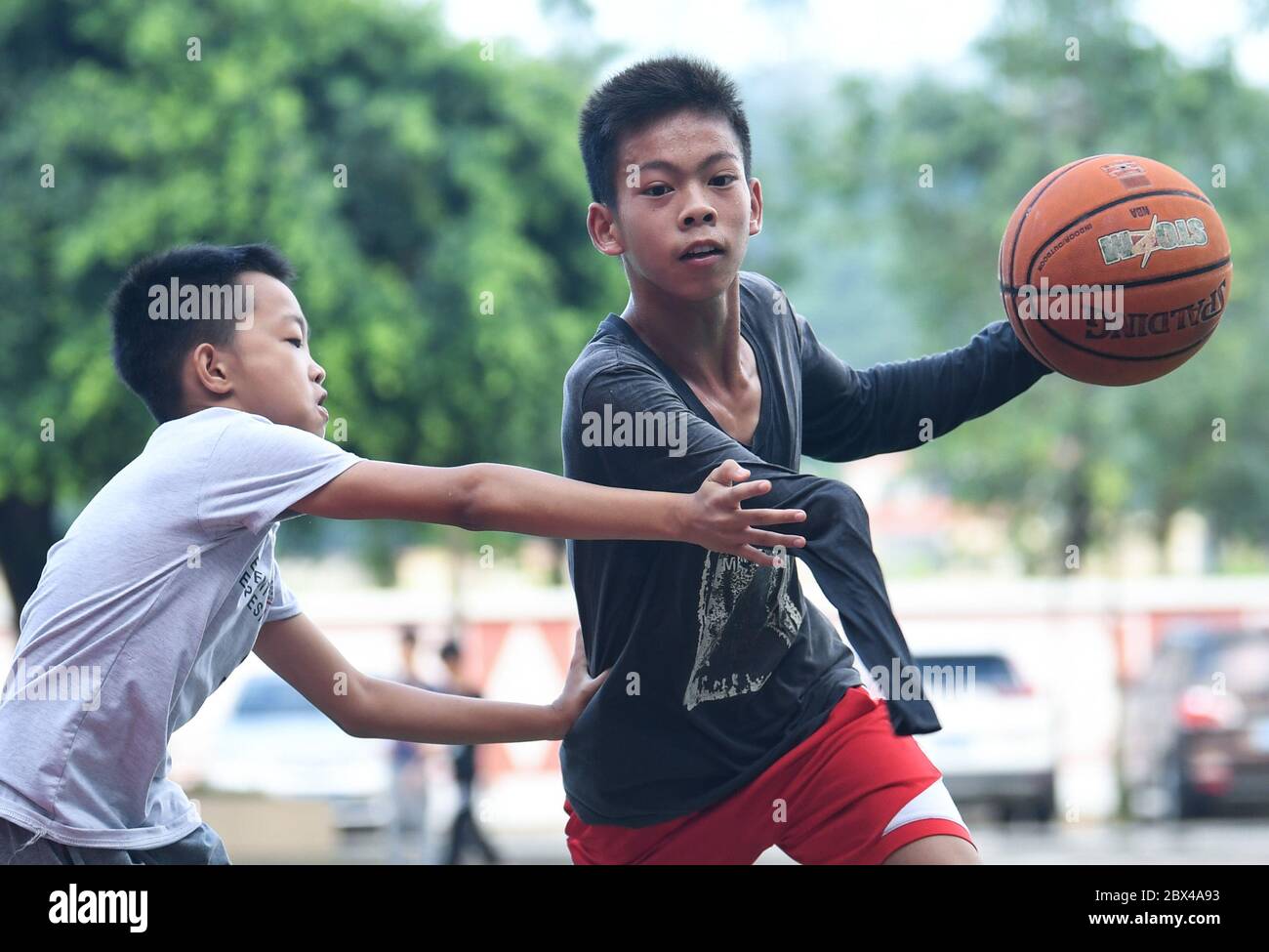 (200605) -- BEIJING, June 5, 2020 (Xinhua) -- Zhang Jiacheng (R) plays basketball with his schoolmate before morning class at a middle school in Gaocun Town of Yunfu City, south China's Guangdong Province, June 4, 2020. Zhang Jiacheng, 14, is a student in his first year of the town middle school. In 2010, the only four-year-old boy lost part of his right arm due to an accidental event. Though stricken by the misfortune, Zhang did not give up his life. In 2018, he met with basketball for the first time during a free basketball training class for children in summer vacation held by local gov Stock Photo