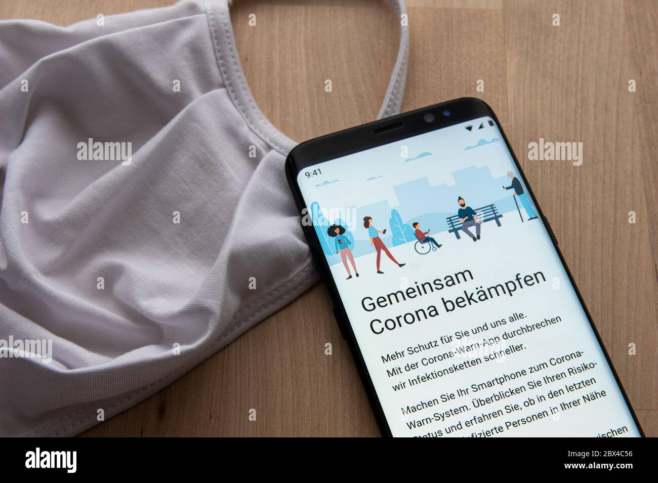 Welcome screen of German Corona Warn App contact tracing with white face mask on wooden surface. Gemeinsam Corona Bekämpfen = German for Fight Corona Stock Photo
