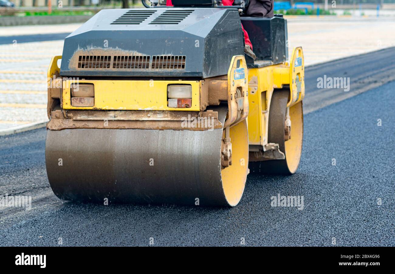 Worker leads the vibrating road roller to compact the asphalt laid out for the construction of a road Stock Photo