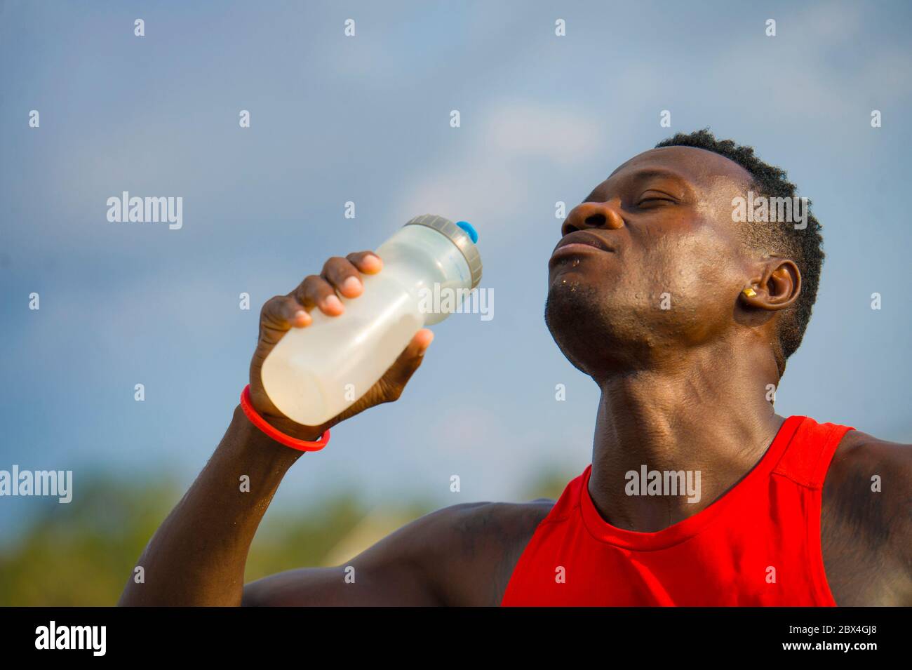 young handsome and attractive black afro American sport man tired and thirsty after running workout holding bottle drinking water or isotonic energy d Stock Photo
