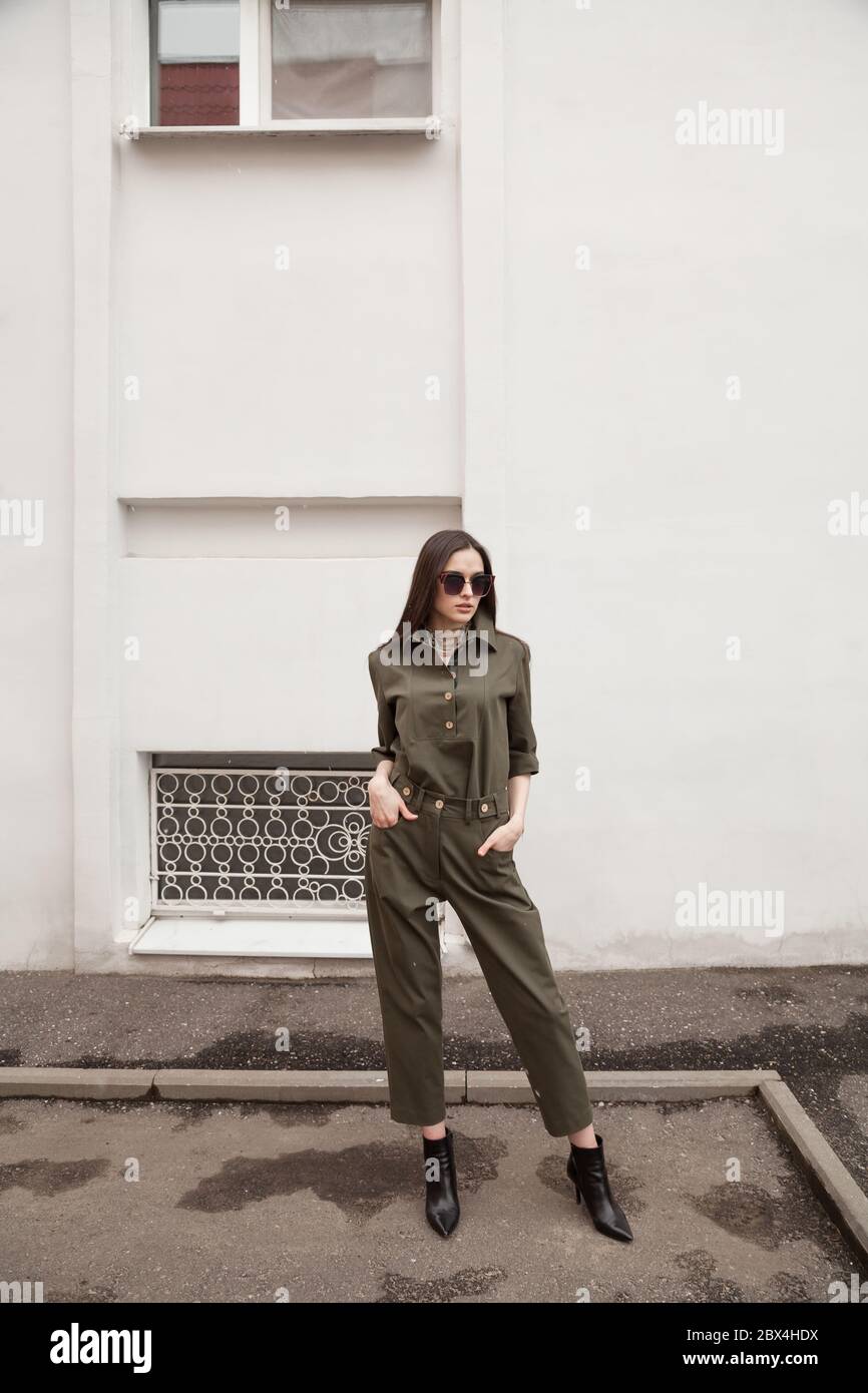 woman wearing green pants suit, posing in street of European city. Copy space Minimalistic white wall urban background, fashion concept, editorial Stock Photo