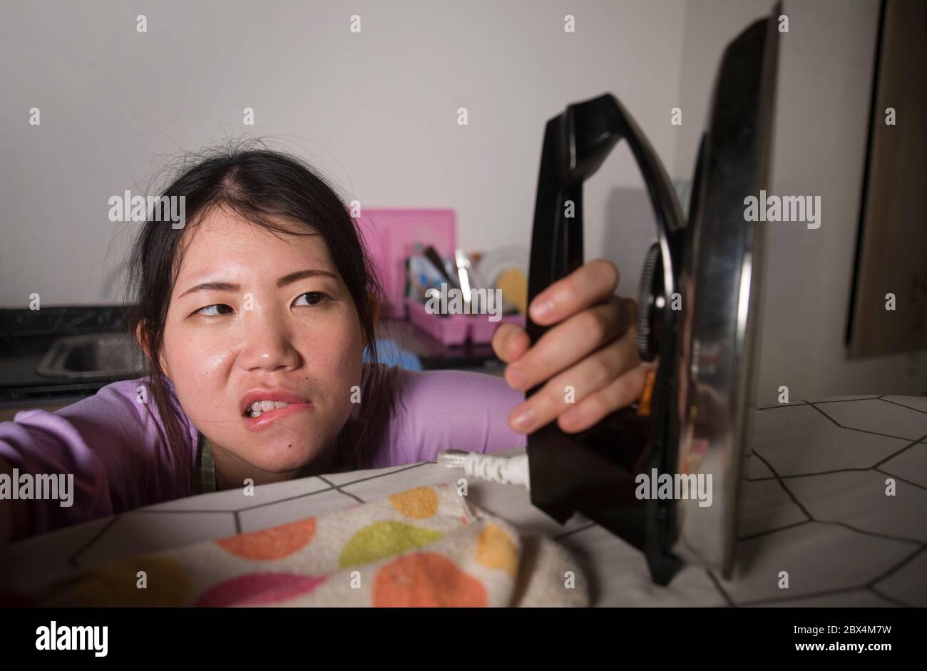 young pretty frustrated and stressed Asian Chinese woman holding iron