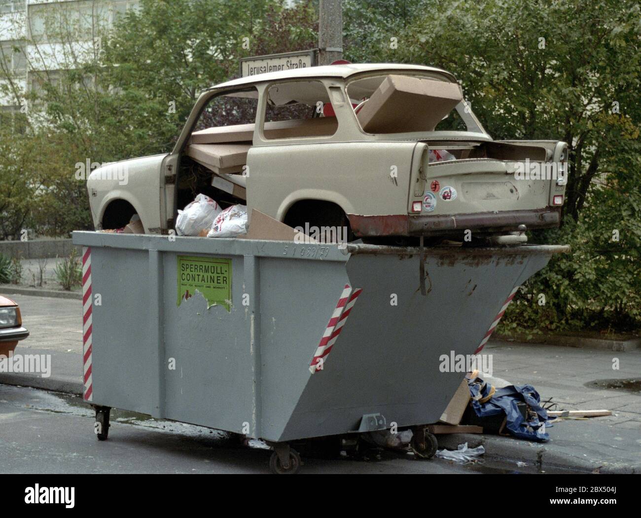Berlin-Mitte / GDR / 1990 A Trabi, symbol of GDR prosperity, is disposed of, near Leipziger Strasse, a symbol for the end of the GDR // Muell / Abfall / Einigung / Wende / Wirtschaft / *** Local Caption *** East Germany / CommunismThe car Trabi-Trabant was the standard car in communist Germany, a sign for moderate wealth. After the unification those cars were only junk, like big parts of the whole economy.the communist symbol in a junk carbage container [automated translation] Stock Photo