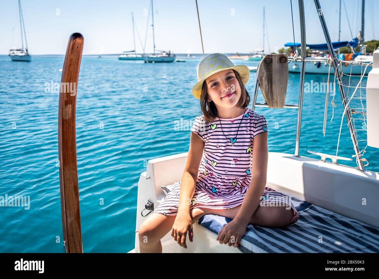 Child on sailing boat yacht summer vacation adventure. Happy girl is enjoying a summer trip on a sailboat moored in an amazing bay in the Adriatic sea Stock Photo