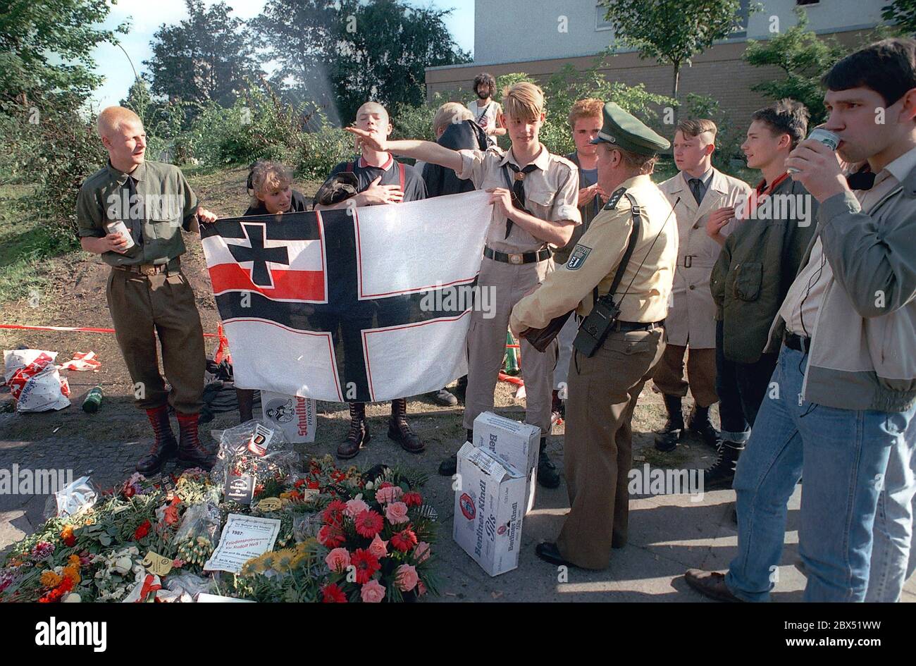 Berlin-Spandau / Nazis / right wing groups 20.8.1987 In front of the war criminals' prison in Spandau, Rudolf Hess has just died. The right-wing groups are gathering in mourning. Young right-wing radical Michael Wendt (right) with the Reich war flag and the Kuehnen salute, a variation of the Hitler salute, which was banned. A policeman inquires what this is all about. Flowers in front for Hess. // Nazi / Fascism / *** Local Caption *** The Prison for war criminals in Berlin-Spandau. The last prisoner, Rudolf Hess, just died after 46 years in the prison shown in the background. Right wing Stock Photo