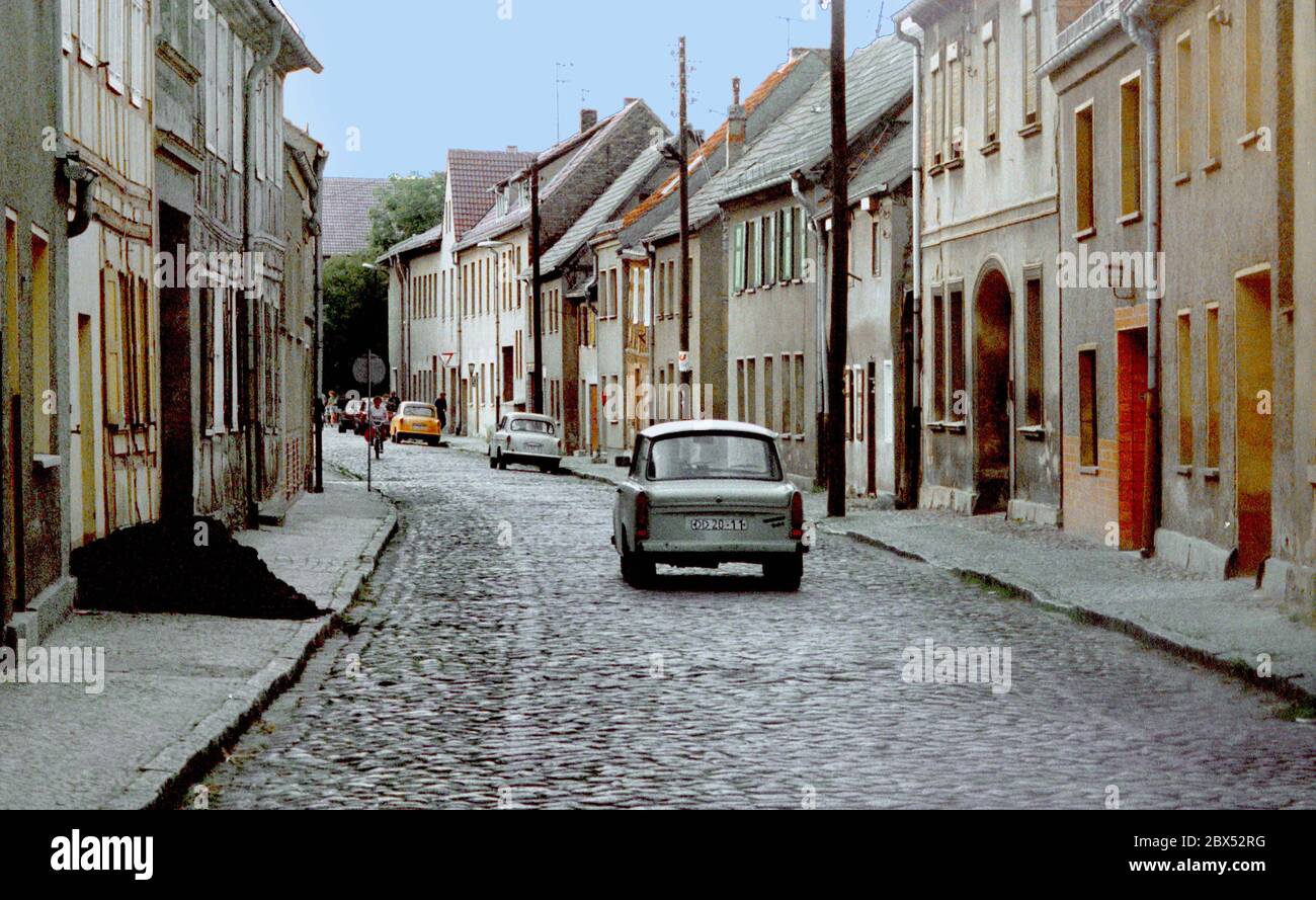 Brandenburg / Teltow-Flaeming Region / GDR / 1990 Jueterbog: Alley with Trabi, in front left a bunch of briquettes. It was usual to simply pour the coal on the street, the customer had to put it in the cellar. // Small town / [automated translation] Stock Photo