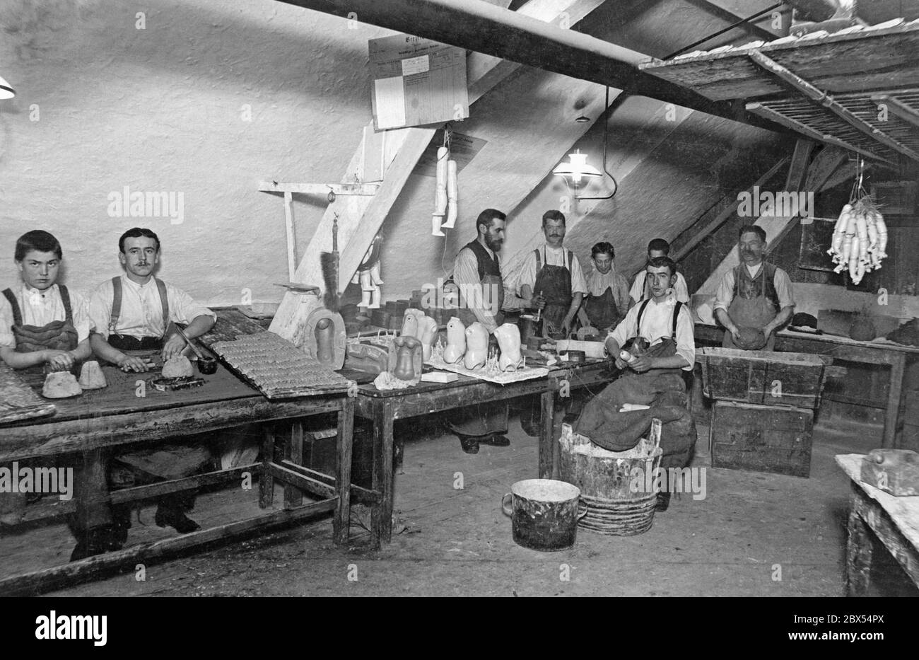 Workers in a Berlin toy factory under the roof at their simple workplaces. They form the individual body parts of the dolls from dough. Stock Photo