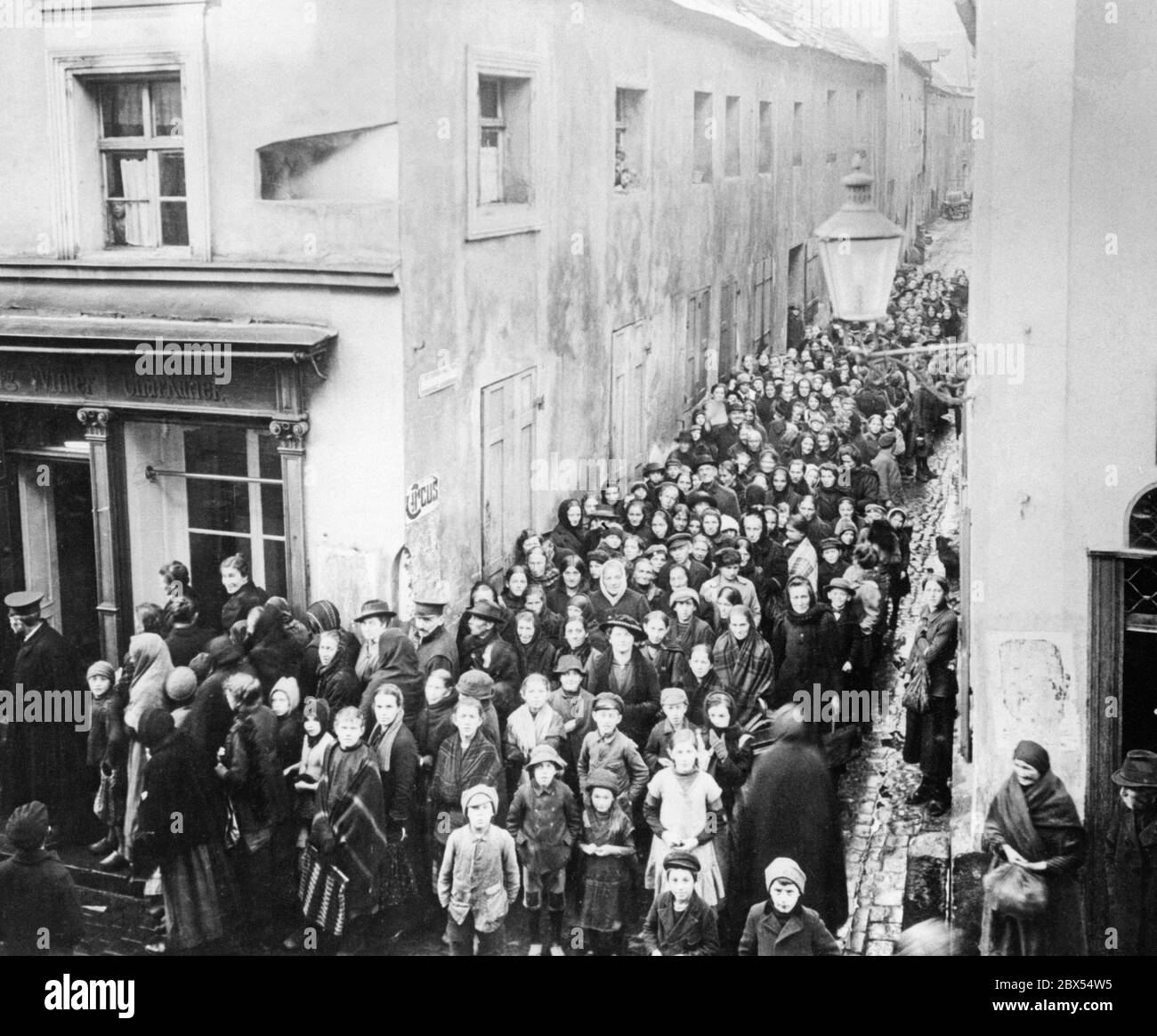 A long queue has formed in front of a bakery in an alley. People are waiting to buy flour. Due to the long war, for which the political and military leadership in Germany did not take precautions, there were supply problems. These culminated in the 'Kohlruebenwinter' ('Turnip Winter') of 1917/1918, in the course of which many old, sick people and children died of exhaustion and malnutrition. Stock Photo