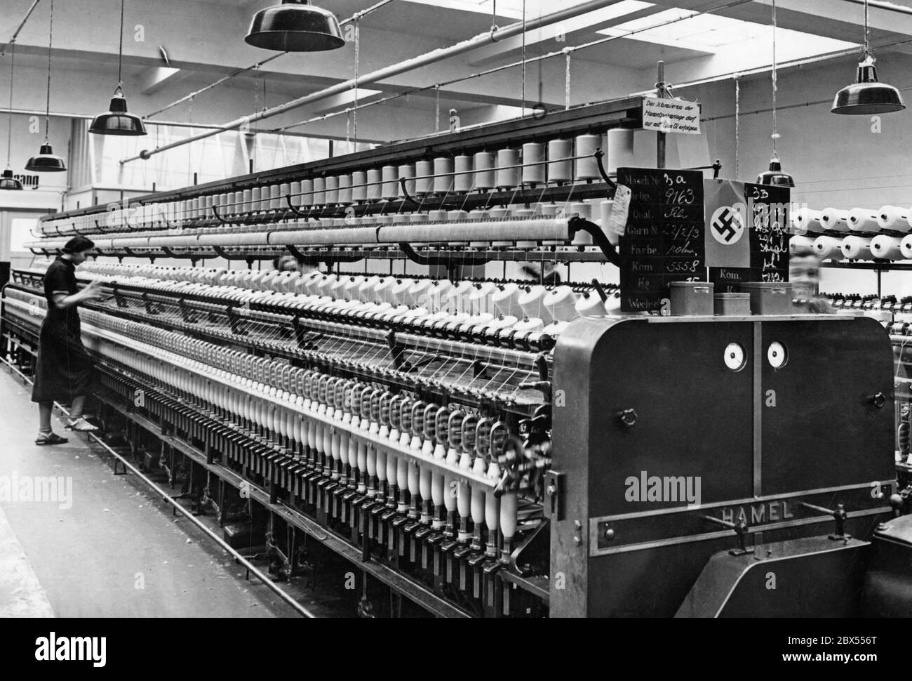 The photograph was taken in Reichenberg (today Liberec), which was part of the Sudetenland annexed in October 1938. It shows the wool spinning mill of the textile factory Liebig & Co, which was equipped with spinning machines considered modern for the standards of that time. On the right side of the machine is a work instruction: 'Lubrication of the Hamel twist rings may only be done with Etna oil'. Stock Photo