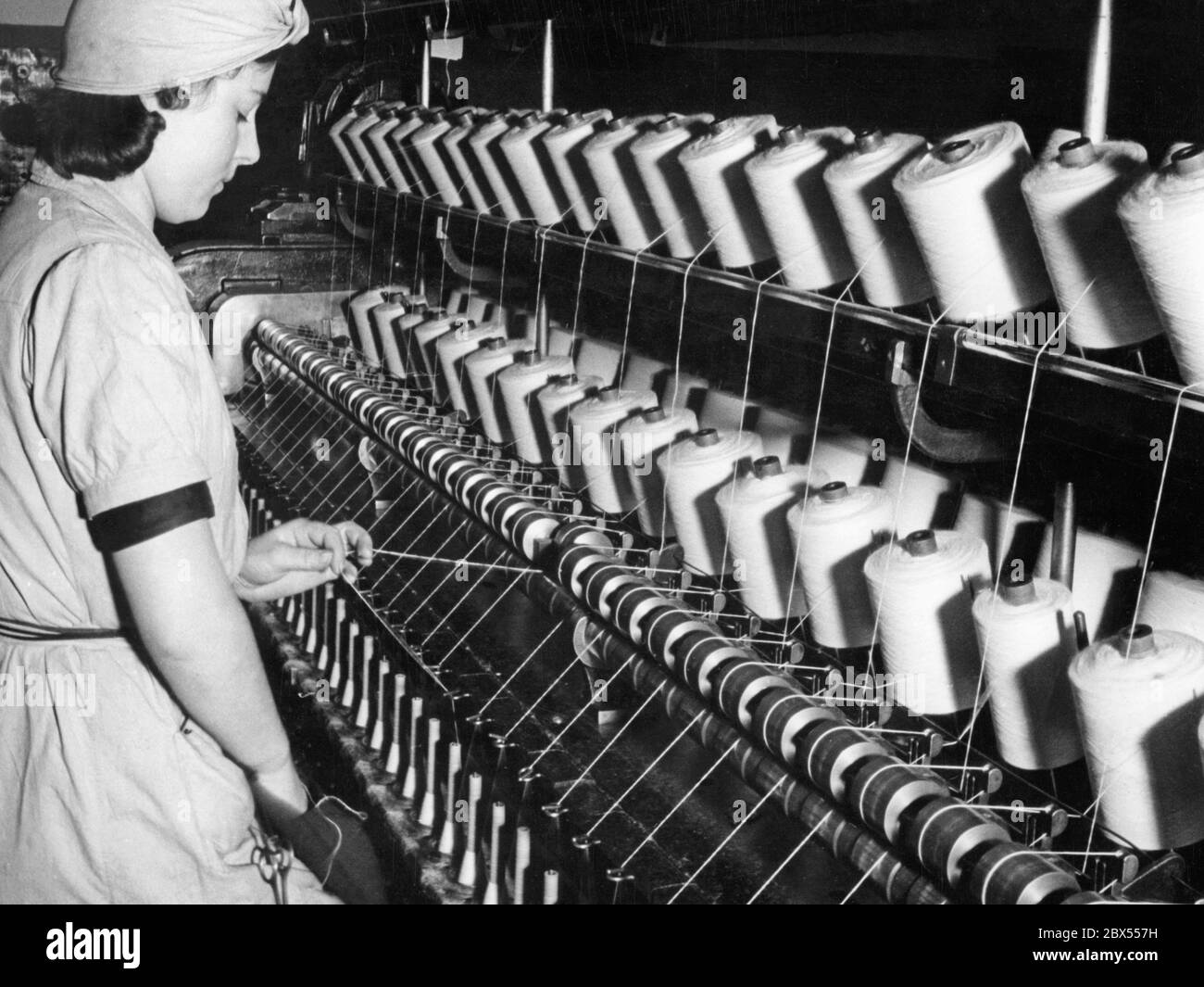 In the spinning school of the Alsatian worsted spinning mill Gluck (or Glueck) & Co. AG from Muehlhausen in Alsace, a woman threads a needle into the ring twisting machine. The photograph probably dates from the 1930s. Stock Photo