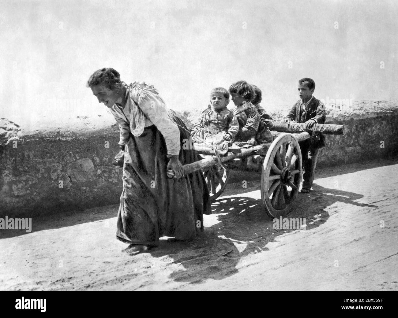 The wife of an agricultural worker in Italy pulls her children on a cart. Stock Photo