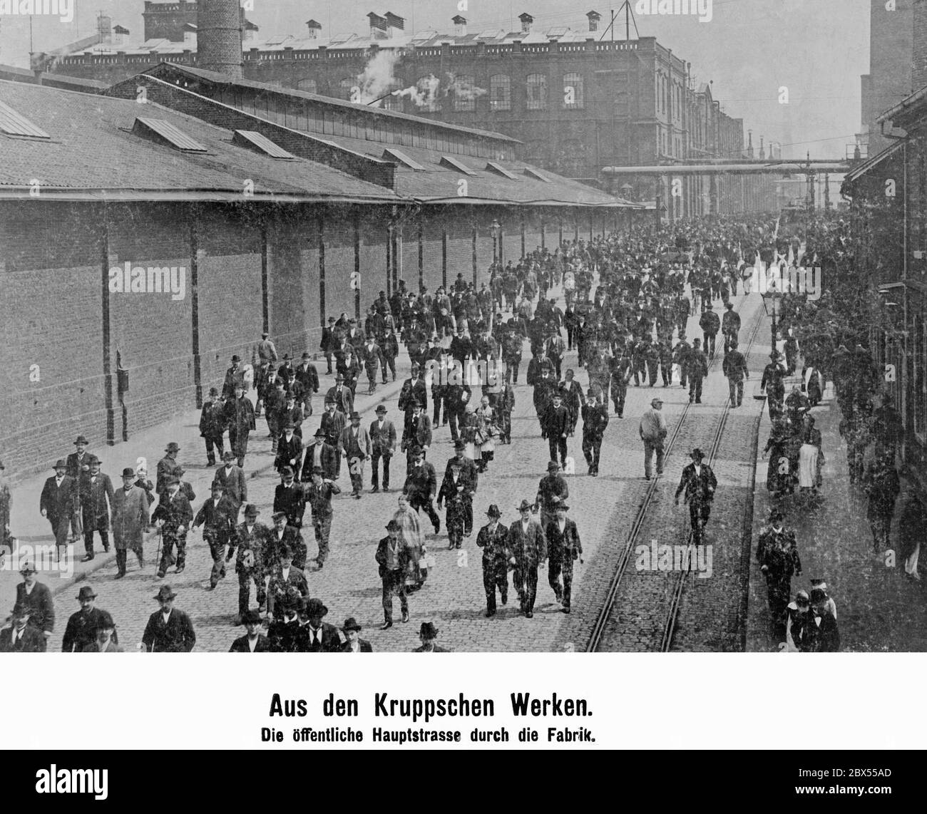 During shift changes in the Krupp works, a crowd of workers walk along the public main road through the factory. Stock Photo