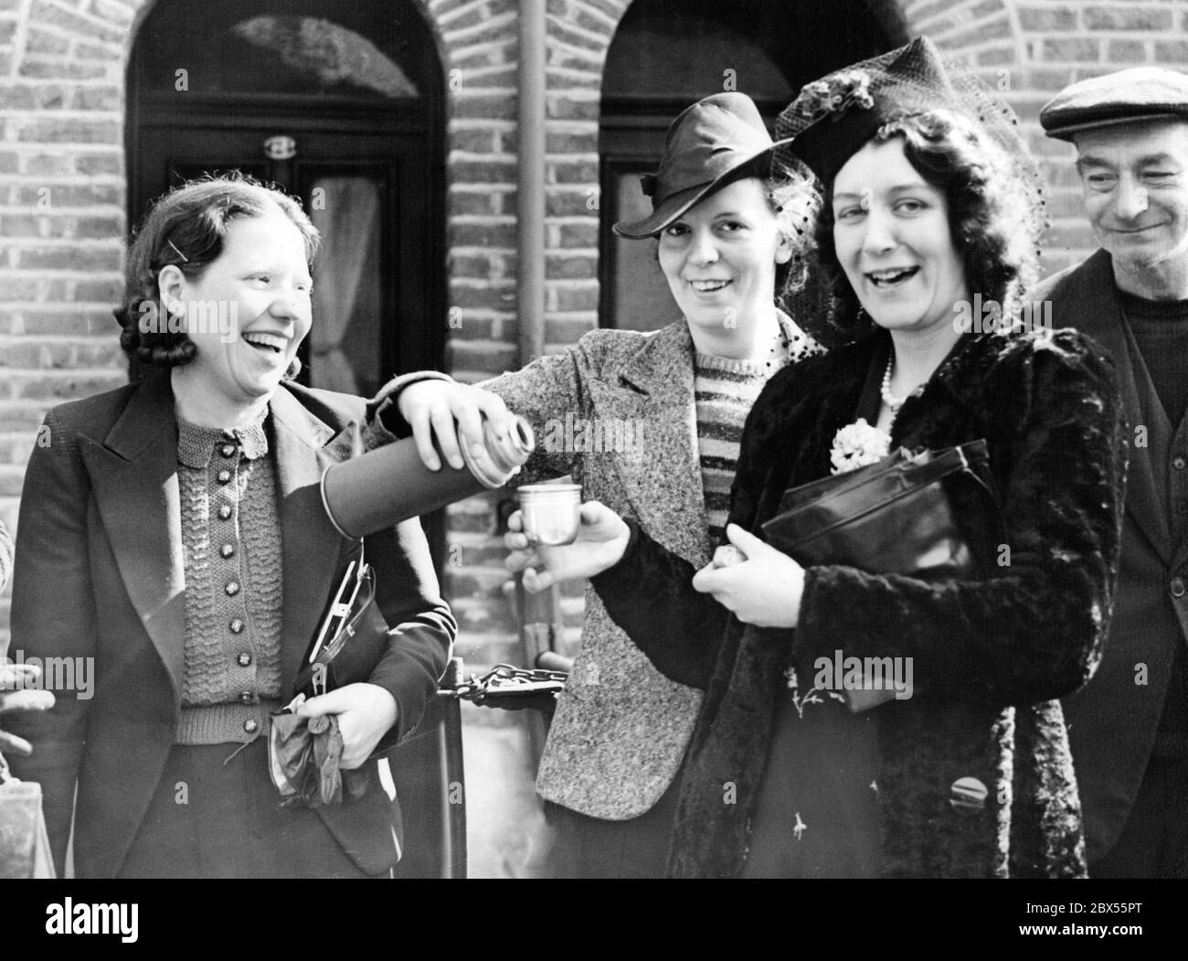Young women refresh themselves with drinks from their thermos flasks in front of the main building of Siemens Brothers & Co, whose employees are on strike after redundancies. Stock Photo