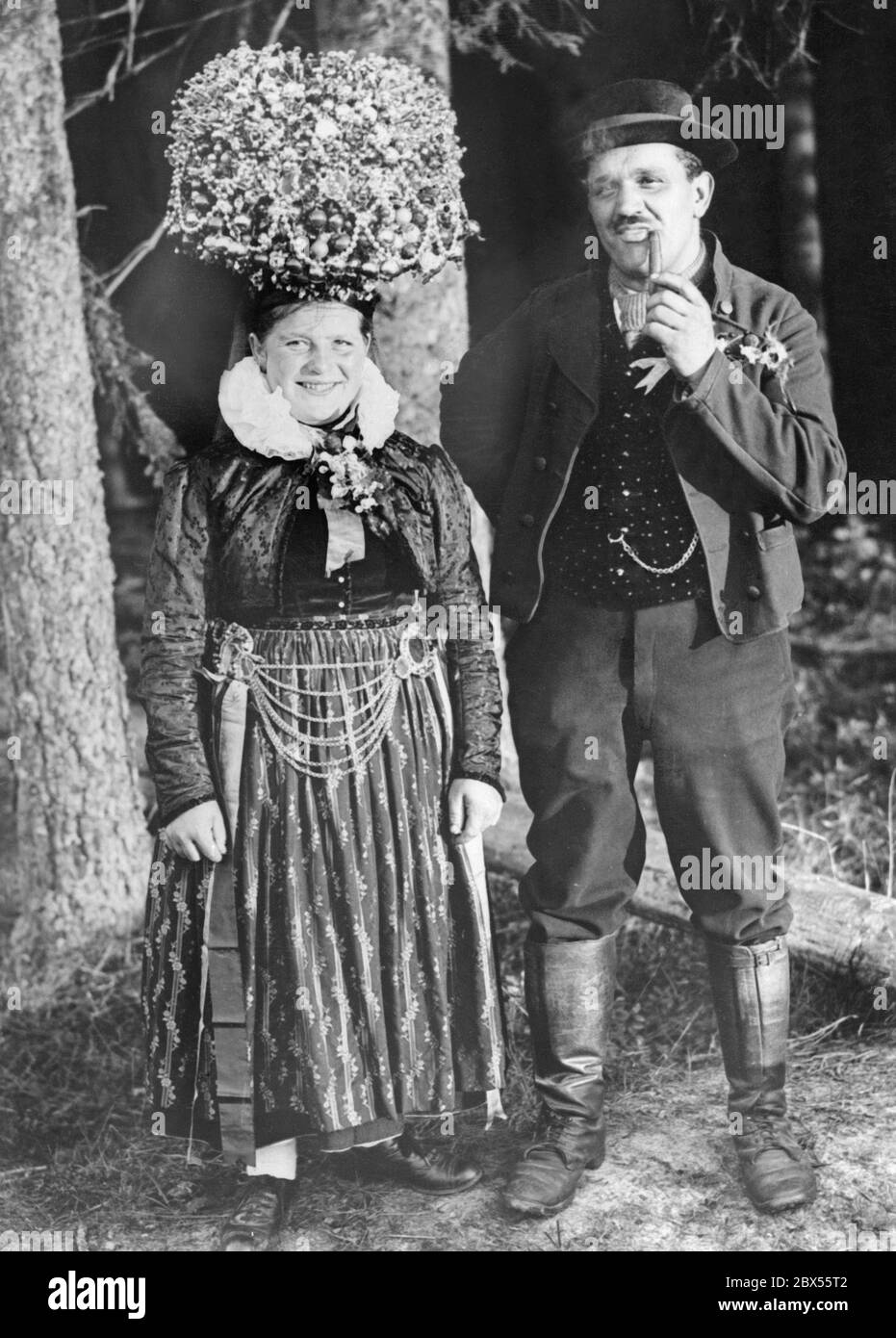 A bridal couple from the Black Forest wear the typical festive folk costume of the region for their wedding. The bride wears a dress and the Schaeppelkrone (bridal crown), a headdress elaborately decorated with glass balls. The man wears leather boots and a vest. Stock Photo