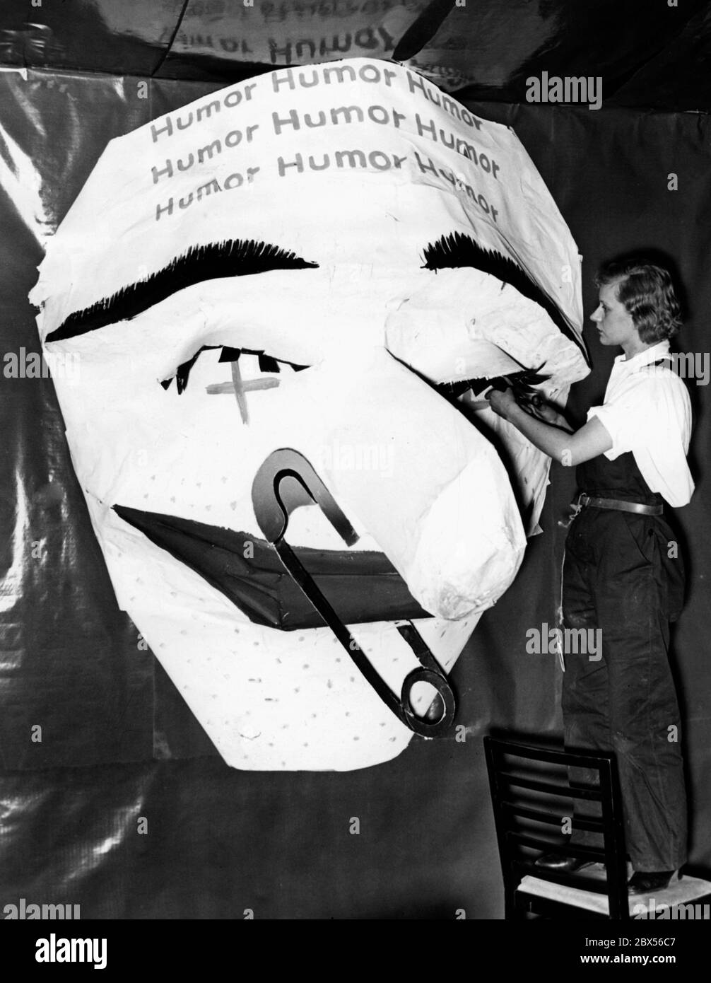 Last preparations for the carnival celebration 'The Night without a Name' at the Haus der Deutschen Presse in Berlin: A wall-decorating giant mask by the artist Will from Halle receives eyelashes as final decoration from a colleague. On the forehead the word 'humor' is visible. Stock Photo