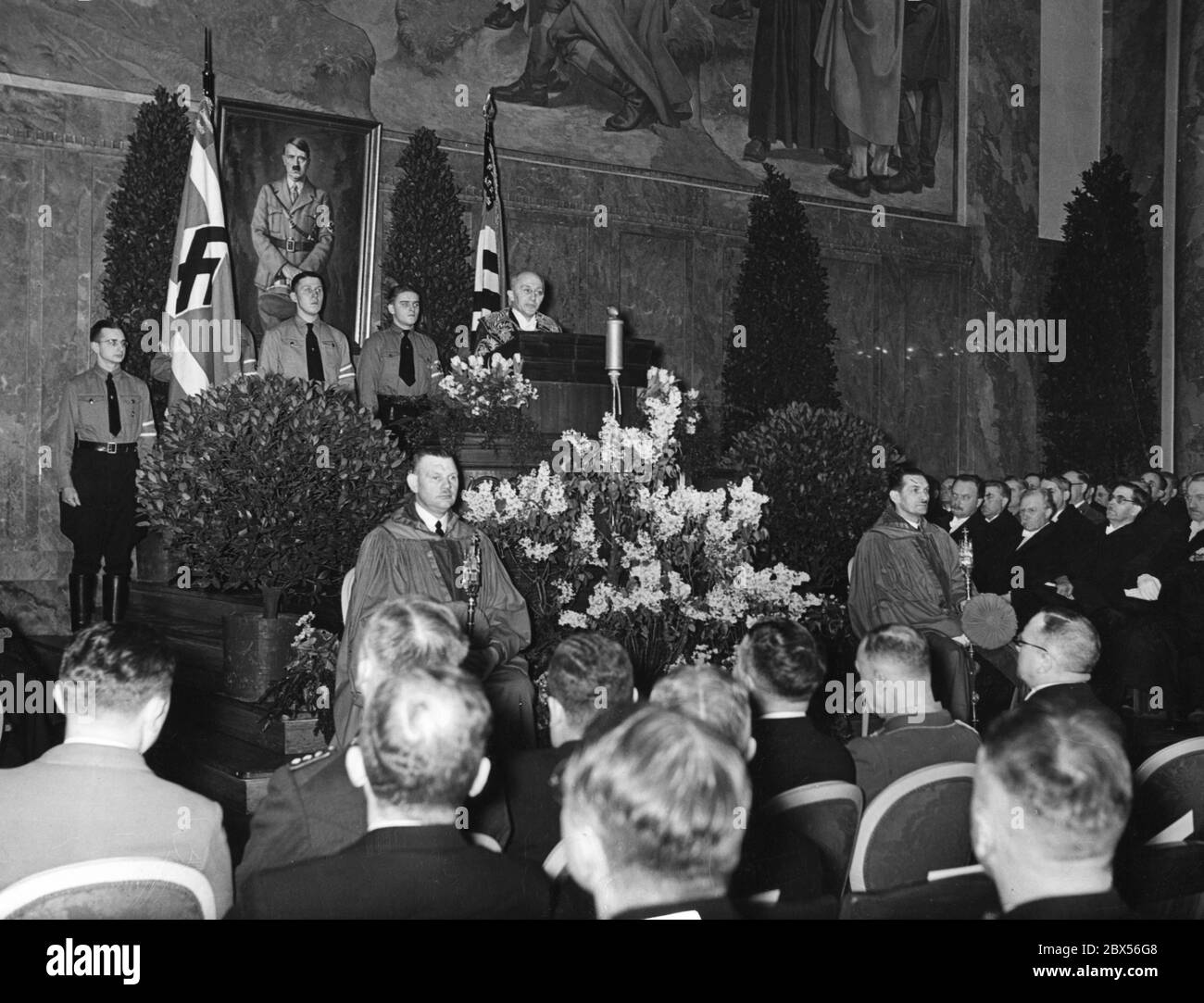 The Rector of the Friedrich-Wilhelms-University Berlin Willy Hoppe (in gown) greets the students at the celebration of the 5th anniversary of the 'Day of National Uprising' in the new auditorium of the university. Behind him is a portrait of Adolf Hitler. On his left is a representative of the NSDStB with flag. Stock Photo
