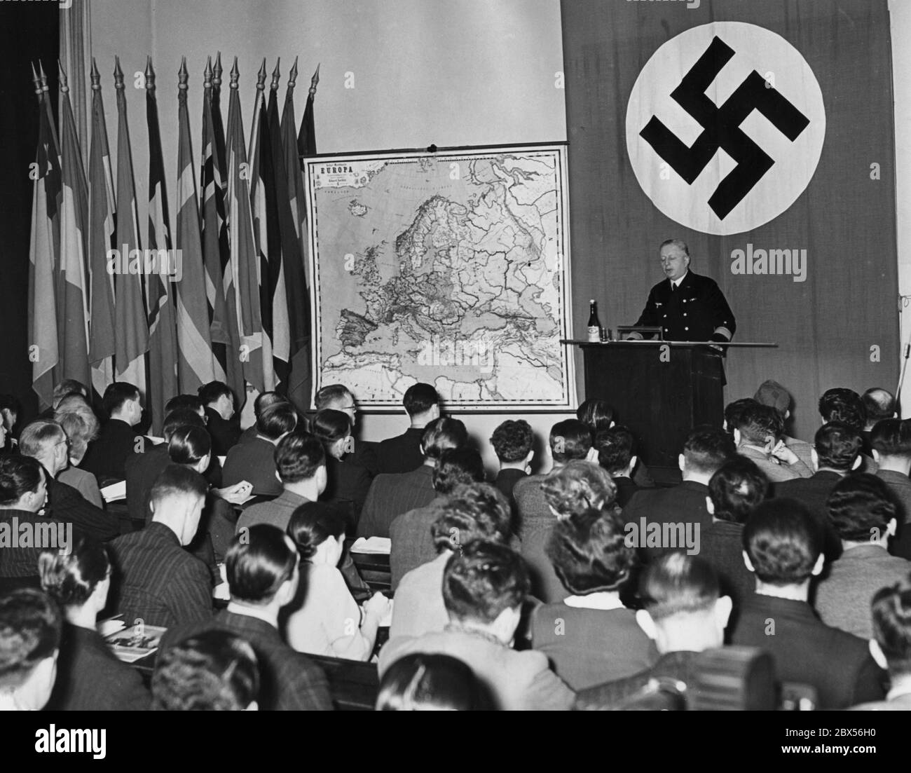 The Institute for International Studies at the University of Berlin organized a holiday course named 'Germany at War', in which more than 200 foreign students from 36 different nations are participating. Here a view into the lecture hall during a lecture by Rear Admiral Gladow. On the wall to the left of a swastika flag is a map of Europe and several national flags. Stock Photo