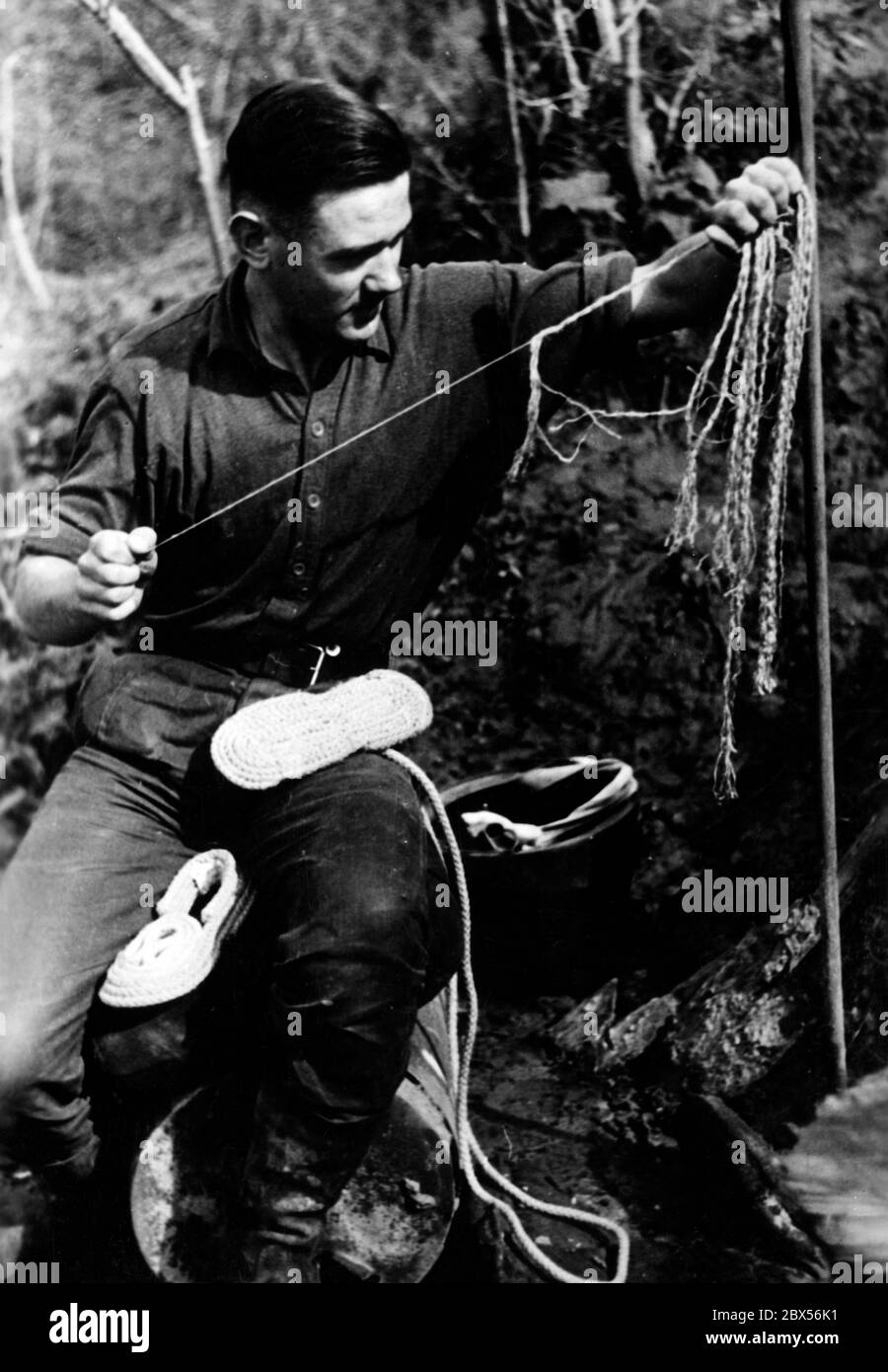 A German soldier makes shoes from the cords of a parachute. During the battle of Kholm, the 'Kampfgruppe Scherer' successfully defended the town for 105 days. (A photo of the Propaganda Company (PK) by war correspondent Richard Muck, who flew into the pocket at the beginning of March). Stock Photo