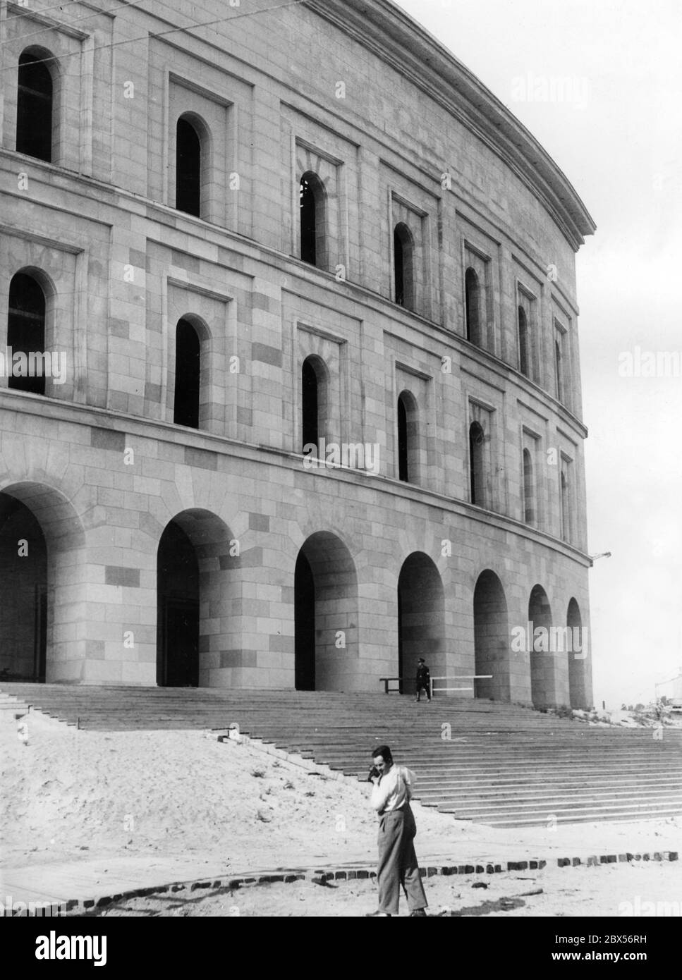 View of the facade of the 40m high model building of the Kongresshalle, designed by the architects Ludwig Ruff and Franz Ruff, before the Reich Party Congress. In the foreground is a photographer, in the background a guard of the SS. Stock Photo