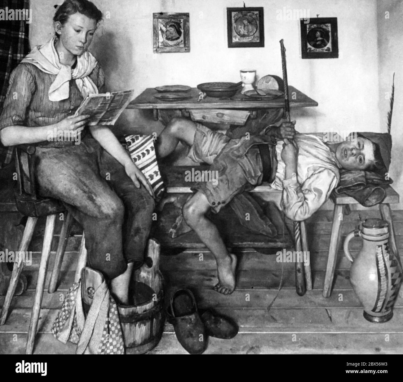 A painting from the works exhibited at the 1940 Venice Biennale. It bears the title 'Nach Feierabend' ('After Work') and is the work of Sepp Hilz. It shows a farm boy and a young girl. Probably siblings. They are in the dining room. The boy lies on the bench while the girl washes her feet while reading a newspaper. On the table there is a light meal. Stock Photo