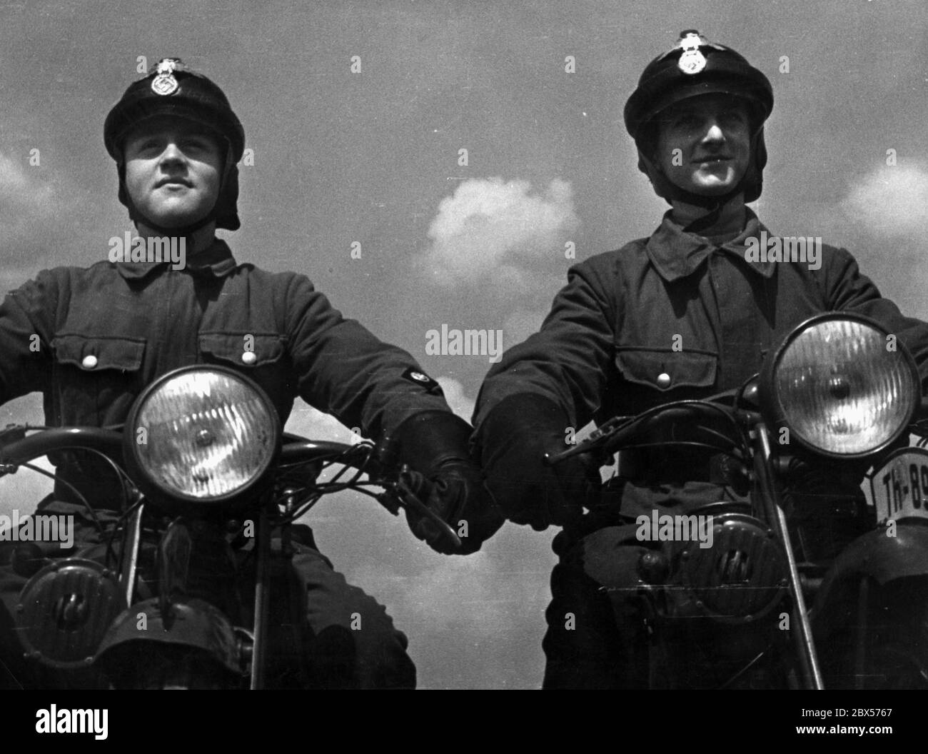 Two members of the Motor Hitler Youth sit on their motorcycles before the ride. They wear helmets. Stock Photo