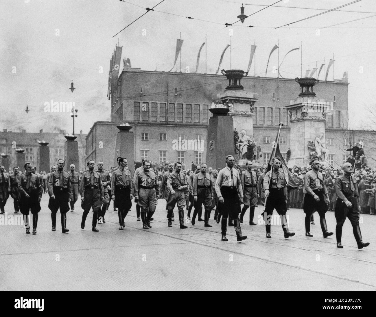Traditional march across the Ludwig Bridge in Munich on the 9th of November in memory of the National Socialists killed in the Hitler coup. Hermann Goering, Adolf Hitler and Ulrich Graf are in the middle of the picture. In the foreground is Julius Streicher. The Blood Flag is carried by Jakob Grimminger. In the background is the Kongresshalle. Stock Photo
