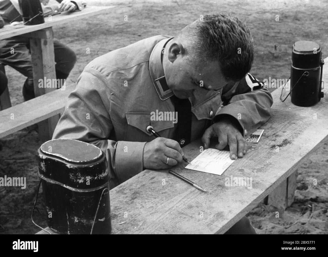 In the tent camp of the Gau Sachsen of political leaders of the NSDAP, a party official writes two postcards from the Reich Party Congress in Nuremberg. Next to him are two cooking containers / cookware. Stock Photo