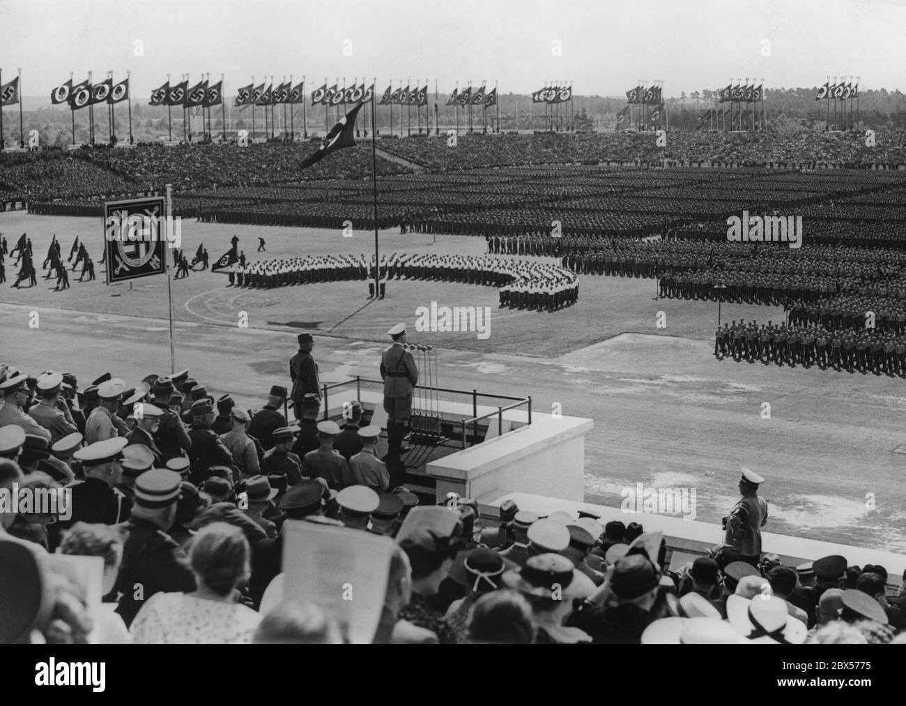Adolf Hitler gives a speech from the pulpit of the Zeppelin grandstand to the approximately 38,000 men of the Reich Labor Service who have taken up their posts. On the left behind him is Konstantin Hierl. On the right side of the picture is the photographer Heinrich Hoffmann. On the left are the RAD flag wavers, in the middle the female youth of the Reich Labor Service. Stock Photo