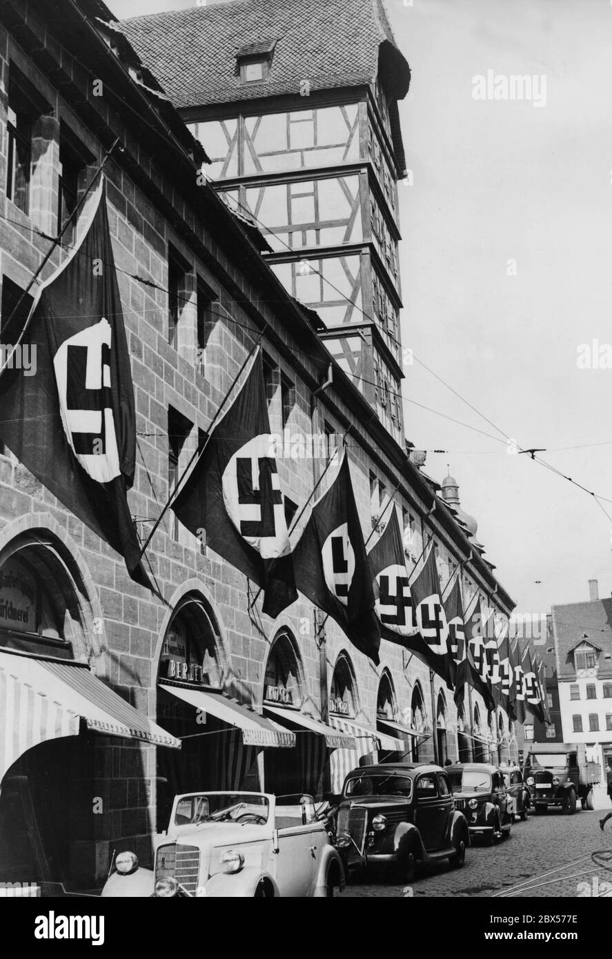 In preparation for the Reich Party Congress, the Mauthalle in the Lorenz Old Town of Nuremberg is decorated with swastika fans. In the foreground are several Mercedes cars. Stock Photo