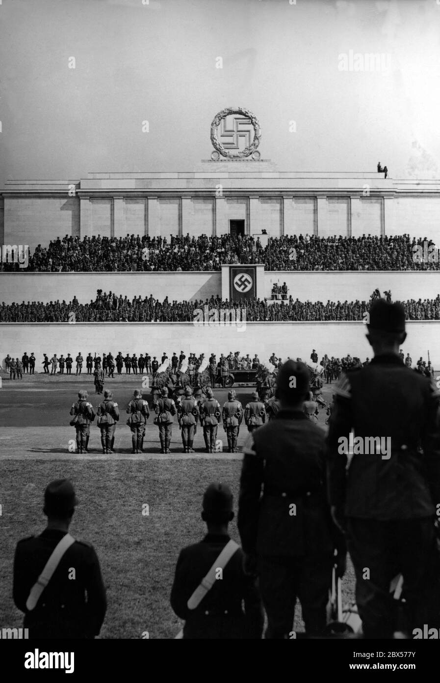 Adolf Hitler, standing in his Mercedes, takes the salute of the formations of the Reich Labor Service on the Zeppelin Field during the Nuremberg Rally. In the background, the Zeppelin grandstand. On the left edge of the picture and on the grandstand are film cameras. Stock Photo