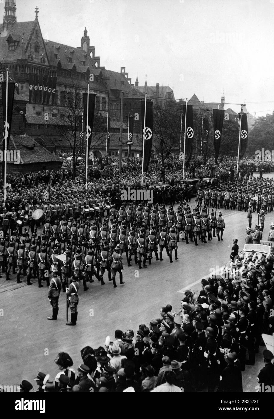 After the presentation of the new police flags on the Deutschherrenwiese, a parade is held in front of the Hotel Deutscher Hof in the presence of Adolf Hitler (in the car on the right side of the picture). In the background the Germanisches National Museum. Stock Photo