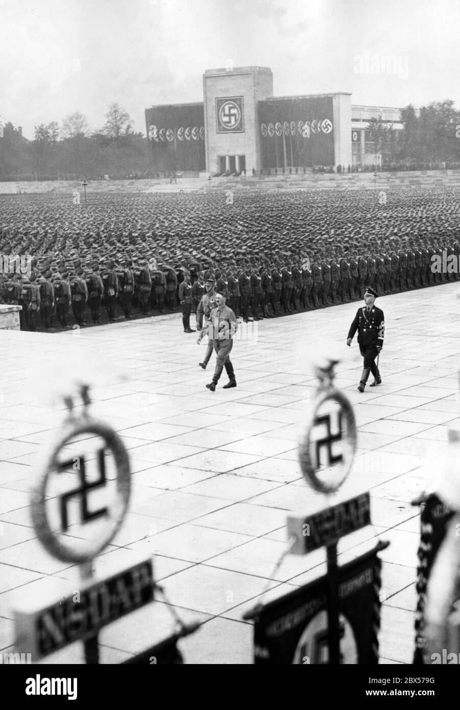 Adolf Hitler (front), Viktor Lutze (left) and Heinrich Himmler (right) march from the platform of the Luitpold Arena to lay the wreath at the Ehrenhalle memorial, during the grand roll call of the SA, SS, NSKK and NSFK. In the background is the Luitpoldhalle. Stock Photo