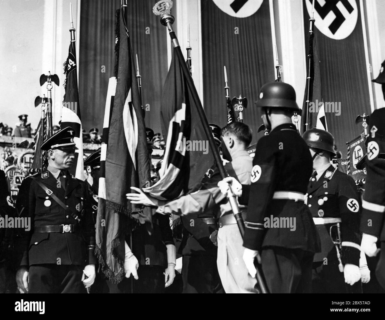 In the rostrum of the Luitpold Arena, Adolf Hitler consecrates new flags of the SS with the help of the Blood Flag. Stock Photo