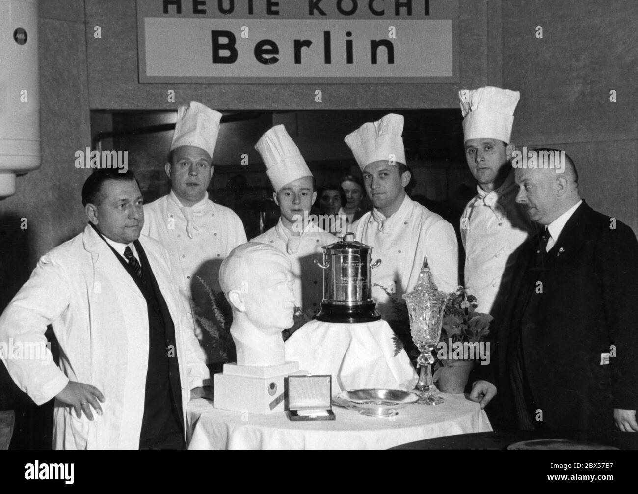 The Berlin chef team has won the 'Golden Marmite' at the 7th International Exhibition of Culinary Art. The head chef has a party badge of the NSDAP and on the table there is a porcelain Hitler head. On the photo from left: Kurt Villbrandt, Peter Saueressig, Paul Oechsler (Eden-Hotel), Wilhelm Rueb (Pauquet), Kurt Moritz (Kaiserhof), Grueger (Gaufachgruppenwalter). Stock Photo