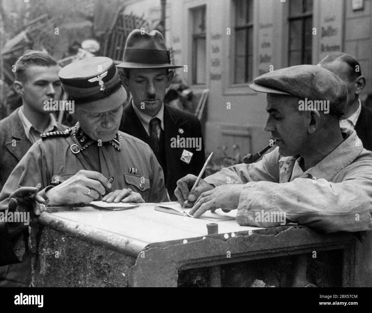 An SA man has his collected scrap metal quantity documented by the scrap material handler. The collection point is located in the Horst Wessel district of Berlin. Stock Photo