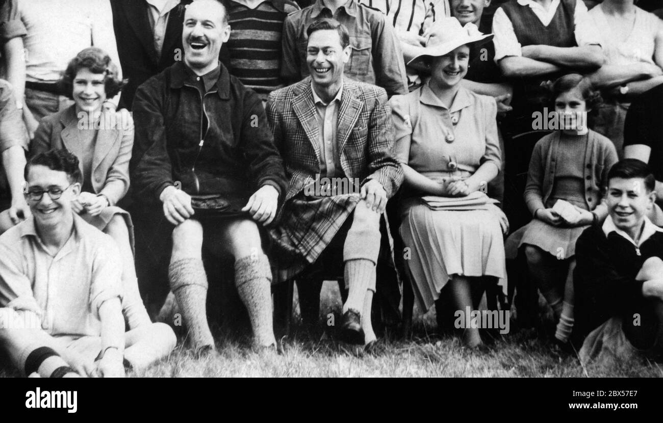 Princess Elizabeth, Captain J.G. Patterson, the camp commander, King George VI, Queen Elizabeth and Princess Margaret Rose watch the boys perform 'Under the Spreading Chestnut Tree' at the Boys Camp. The King is wearing a traditional grey Balmoral Kilt. Stock Photo