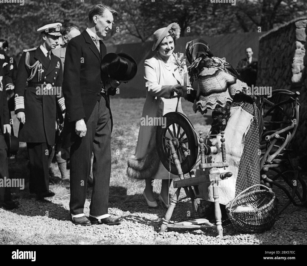 Queen Elizabeth shakes the hand of Maidie Morrison, a woman with a spinning wheel from Barra, during the Empire Exhibition in Bella Houston Park in Glasgow. King George VI ( left behind ) is accompanying her. Stock Photo