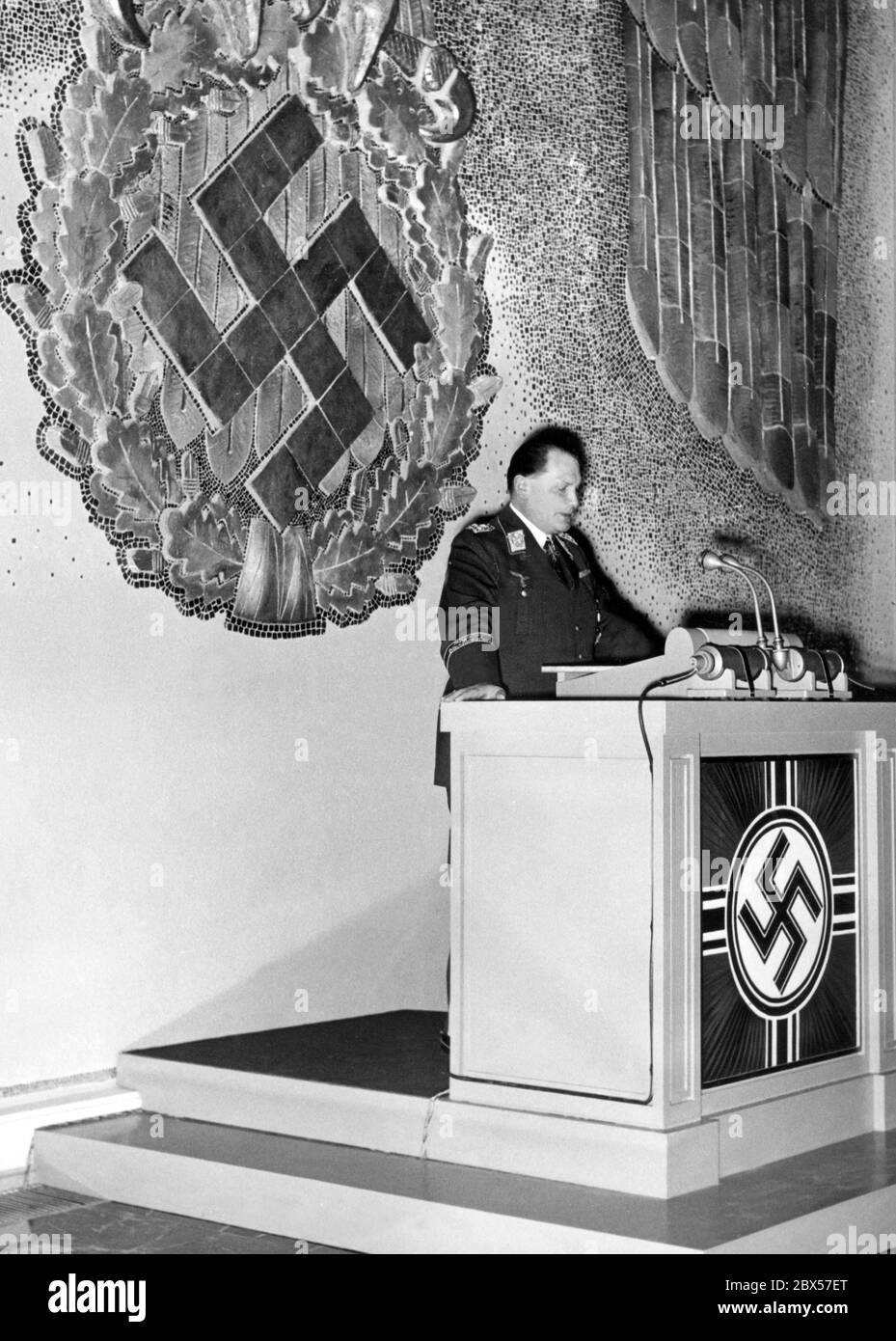 Hermann Goering, in Luftwaffe uniform, gives a speech at the opening ceremony of the Deutschen Akademie der Luftfahrtforschung (German Academy of Aeronautical Research), where he served as president, at the Reichsluftfahrtministerium (German Ministry of Aviation). On the wall behind him, in typical pompous style, there is a tiled swastika in the claws of the Imperial Eagle. Stock Photo