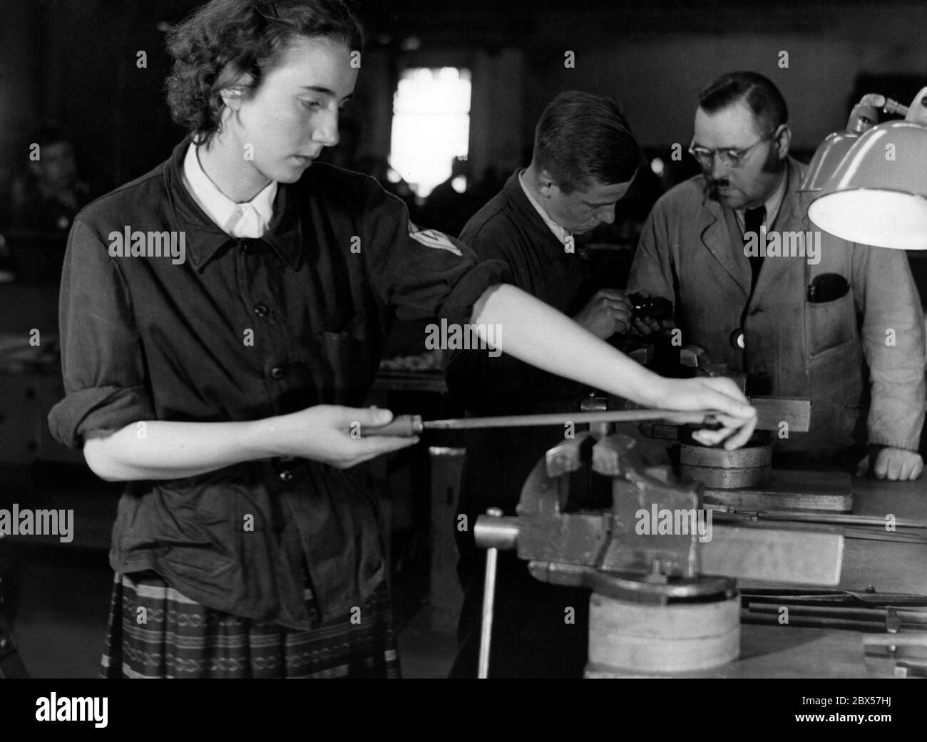 Before her training in drawing, an air-raid warden is given a short practical training in the apprentices' training shop. Here, she practices with a file. Stock Photo