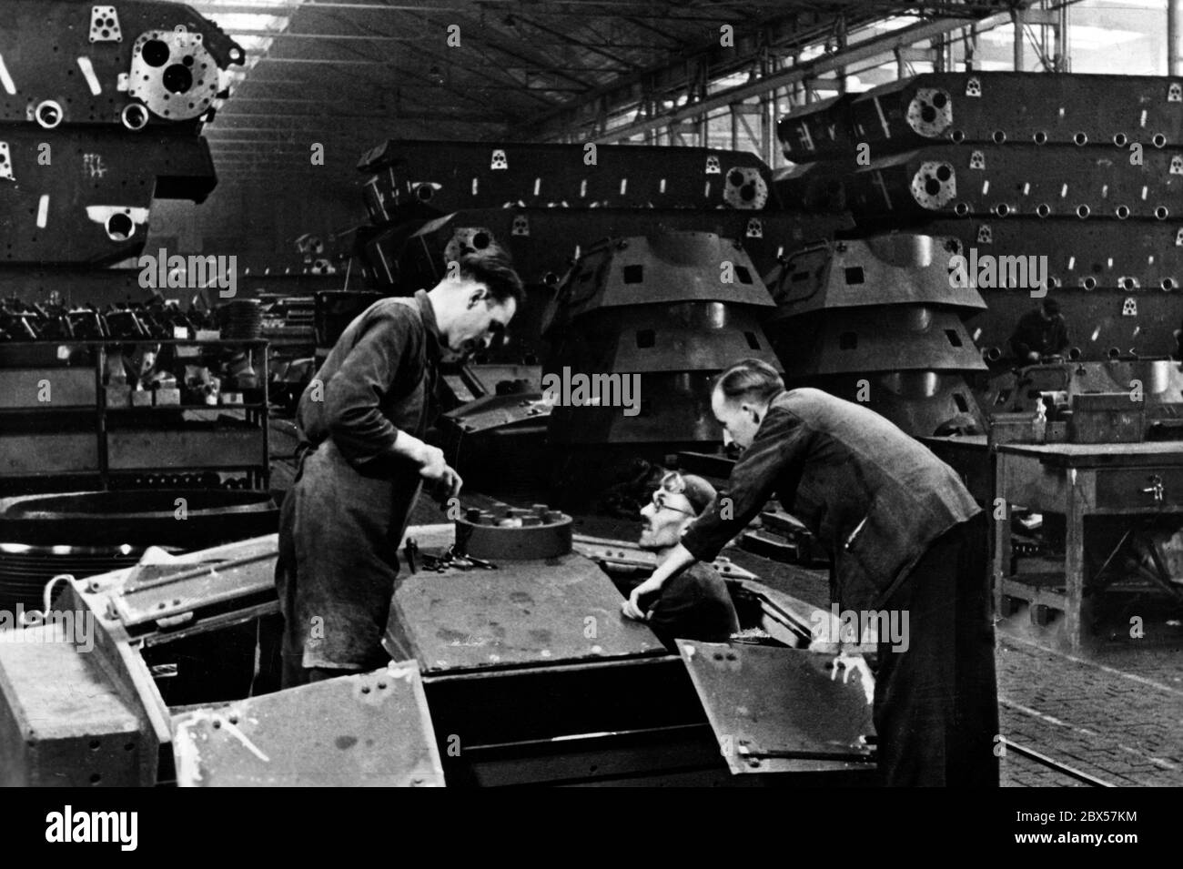 Employees of Rheinmetall manufacture a tank turret, in the background, tanks and turrets are piled up ready for the next production stage. Stock Photo
