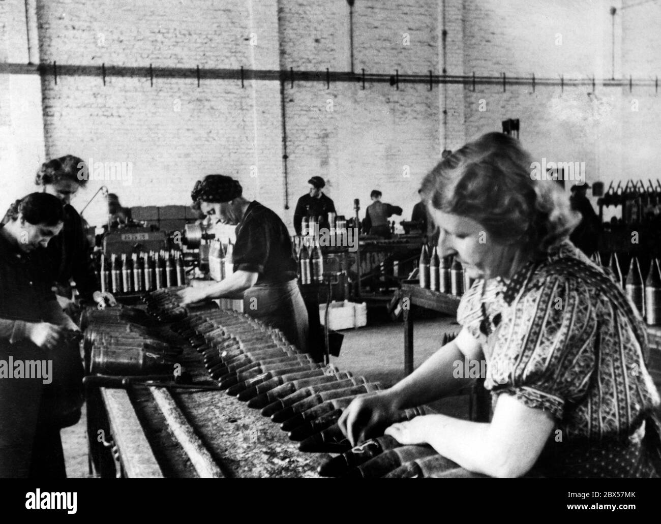 The propagandistic tone on the back of the picture already indicates the end of the war. In the armaments industry, women also have to work at full capacity to ensure supplies for the Wehrmacht during the second half of 1944. Stock Photo