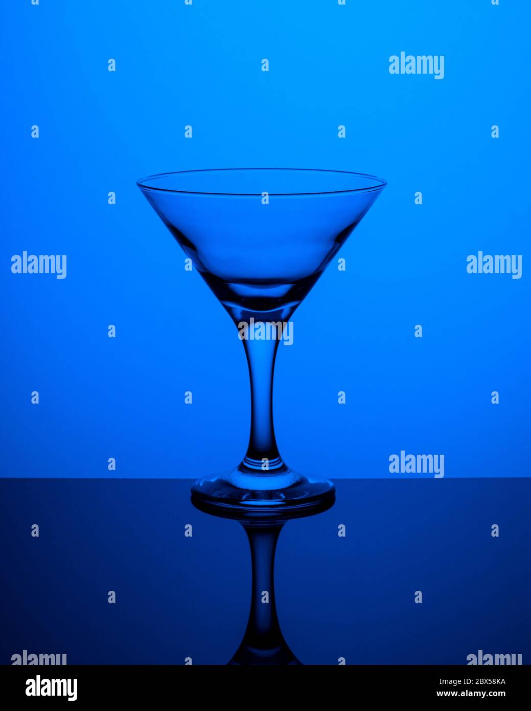 Glass goblet without wine on a thin leg stands on a mirror surface