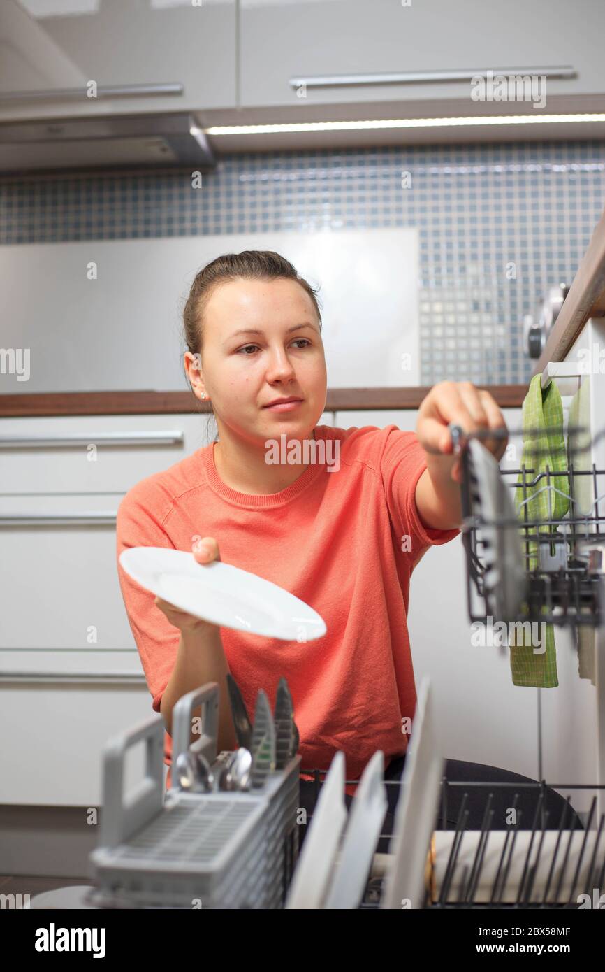 Pretty young woman putting some kitchen equipment to dishwasher