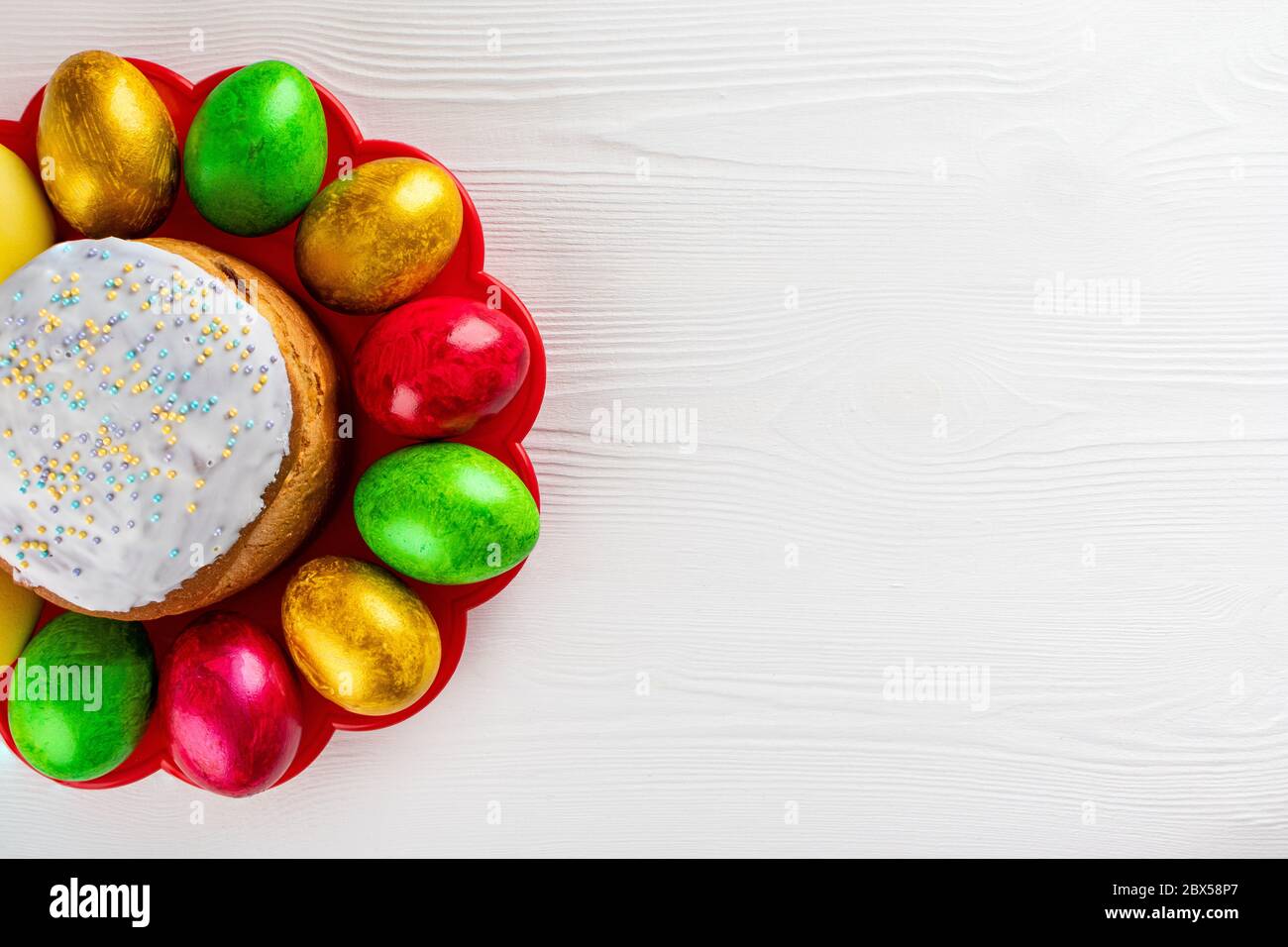 Easter cake kulich. Traditional Easter sweet bread and easter colorful eggs on plate on white wooden background. Copy space. Stock Photo
