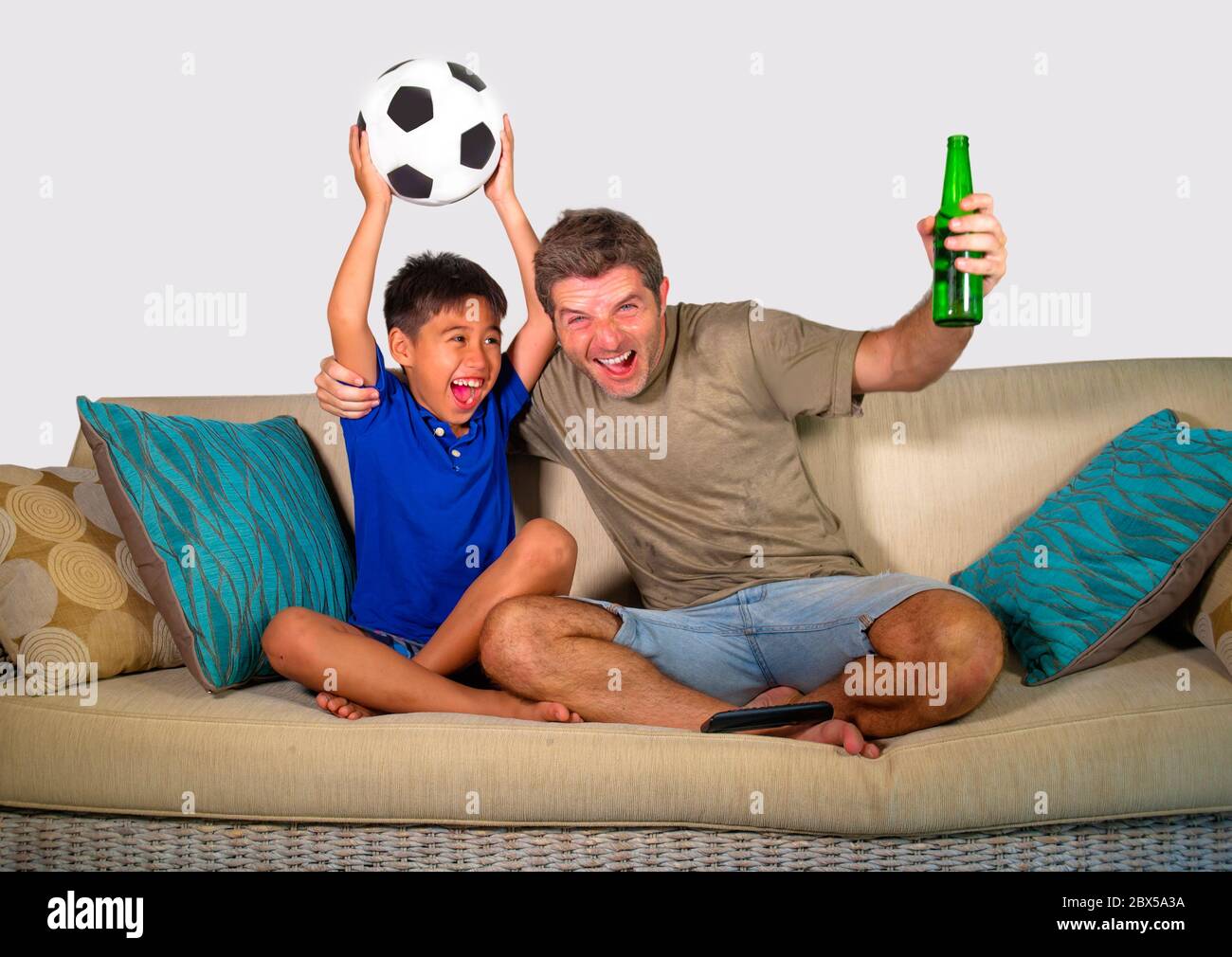 young football fan father and little son celebrating goal and victory happy and excited watching football game on television at home sofa couch gestur Stock Photo