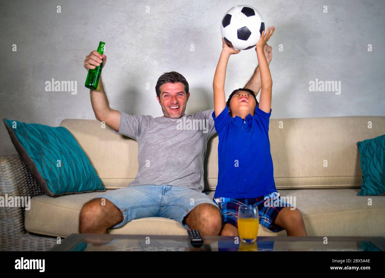 young football fan father and little son celebrating goal and victory happy and excited watching football game on television at home sofa couch gestur Stock Photo