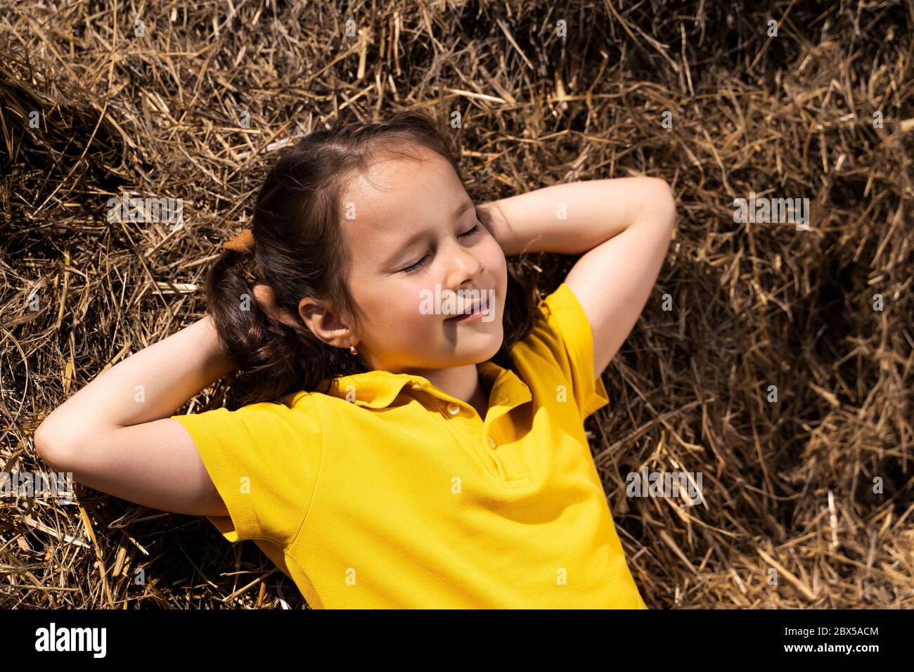 a beautiful girl in a yellow t shirt is lying in the sun in the hay Stock Photo