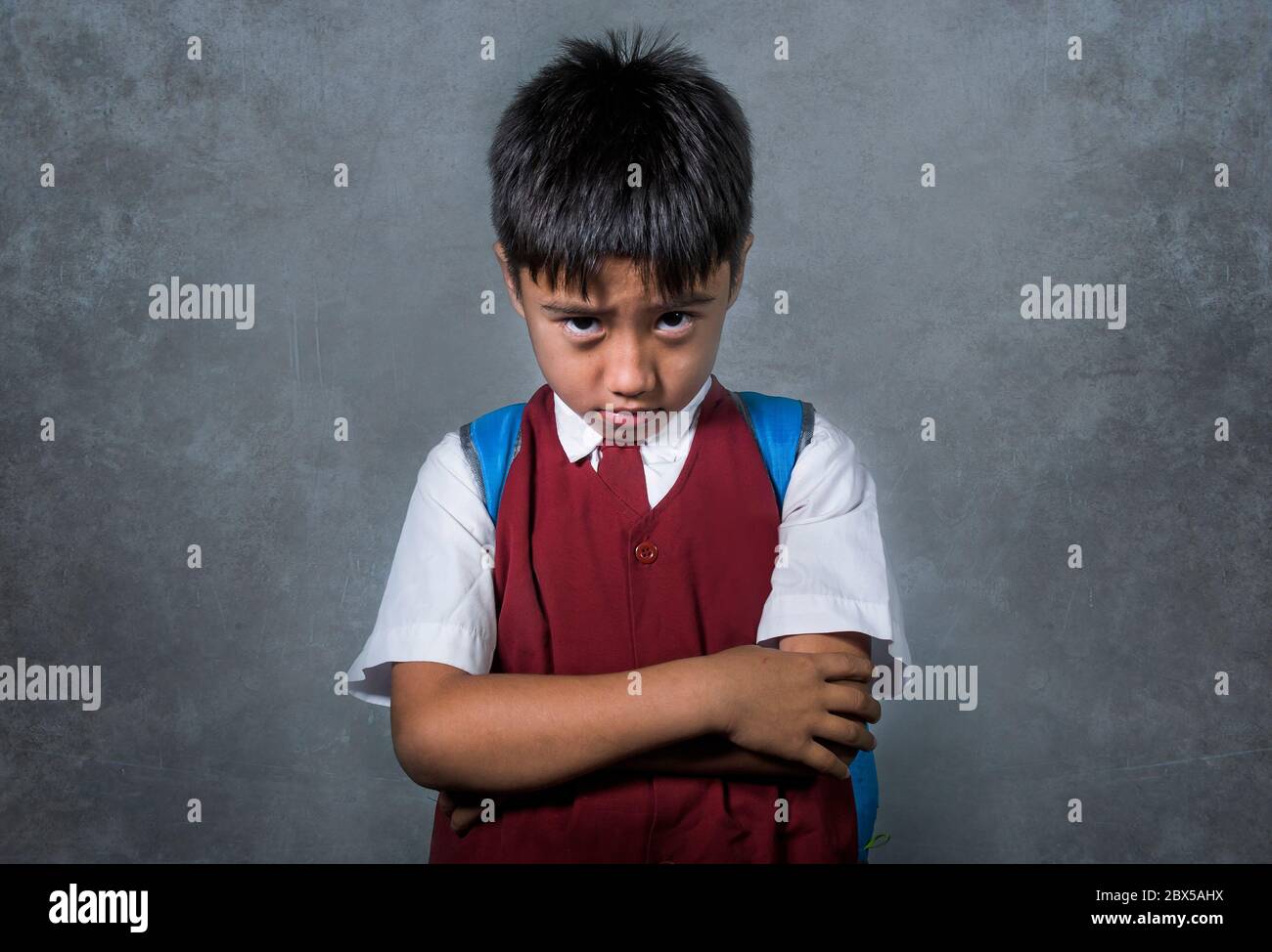young bullied and abused schoolboy in uniform carrying school bag sad