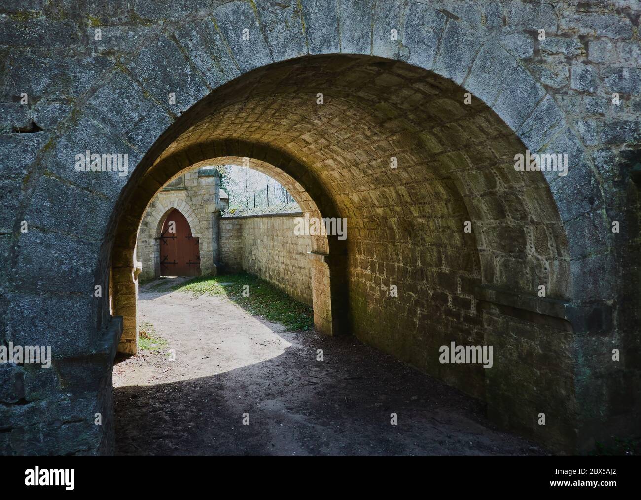 Dark arcade of roughly hewn stones with bright sunlight at the exit Stock Photo