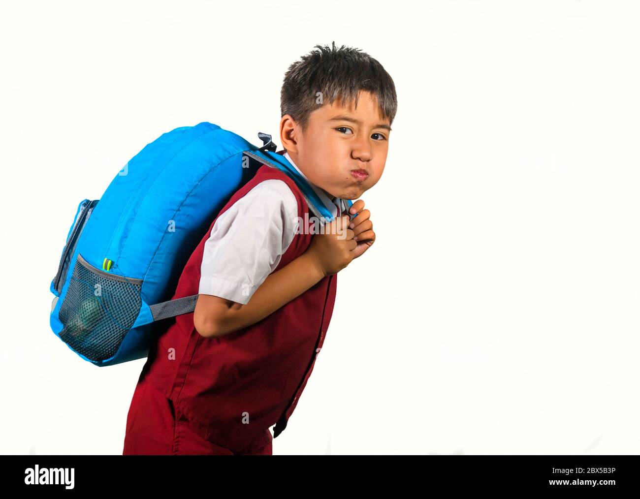 7 or 8 years old sweet kid in uniform carrying bag full of books feeling upset and complaining about the weight of the backpack in lazy schoolboy unha Stock Photo